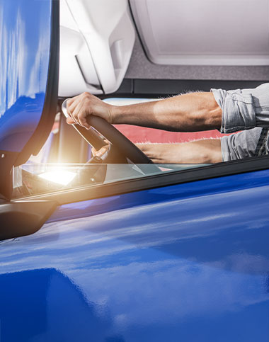 Una persona conduce un vehículo azul con las manos firmes en el volante, visto a través de la ventanilla lateral, pasando junto a la histórica apertura de puertas de Cádiz.
