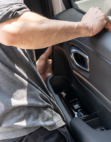 Una persona con camisa gris mete la mano en el bolsillo de la puerta de un coche, con la abertura ligeramente abierta, capturando la esencia de la apertura de coches en Cádiz.