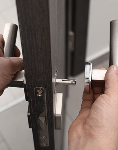 Manos instalando un tirador de plata en una puerta de madera oscura, mostrando la fina artesanía de "Apertura de puertas en Cádiz.