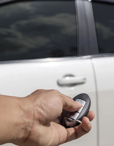 Una mano que sostiene el llavero de un coche, lista para la acción, apuntando hacia un coche blanco con las ventanas cerradas: una escena perfecta para quienes buscan apertura de coches en Cádiz.